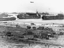 U.S. Navy LSTs and other vessels unloading at low tide at Normandy, soon after the June 1944 invasion. USS LST-55 is in the center, behind the closest barrage balloon. USS LST-61 is at right.